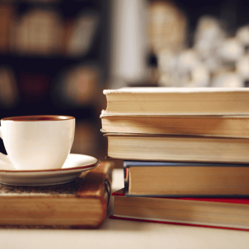 A cozy scene features a stack of books beside a cup of coffee in a warm, softly lit setting, inviting relaxation and reading.
