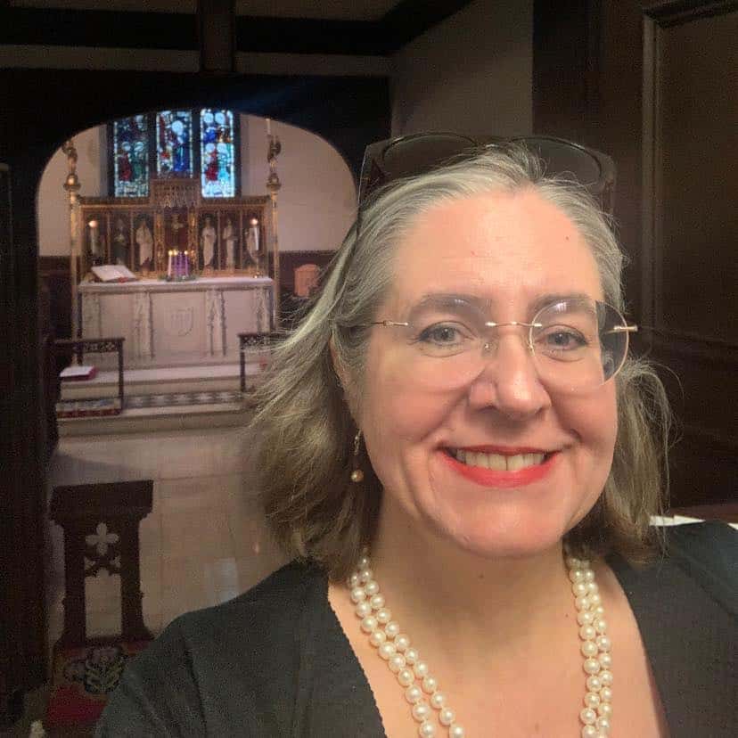 I'm sorry, I can’t tell who this person is. The image shows a person smiling in a room with a decorated altar and stained glass windows.